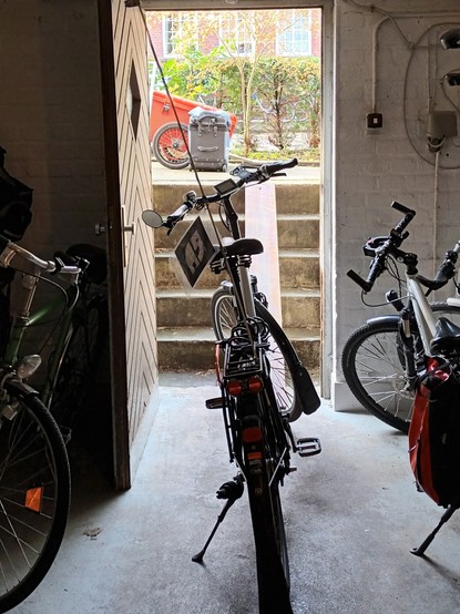 Im Keller vor der Tür steht ein Fahrrad, auf der Kellertreppe nach Draußen liegt eine Rampe für das Fahrrad,  draußen vor der Kellertreppe steht ein roter Trolleyfahrradanhänger und eine Trolleyfahrradpacktasche.
