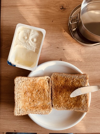 Frühstücksteller mit zwei Scheiben Toast und einer Schale Frischkäse in der man einen comicartigen Gesichtsausdruck erkennen kann.